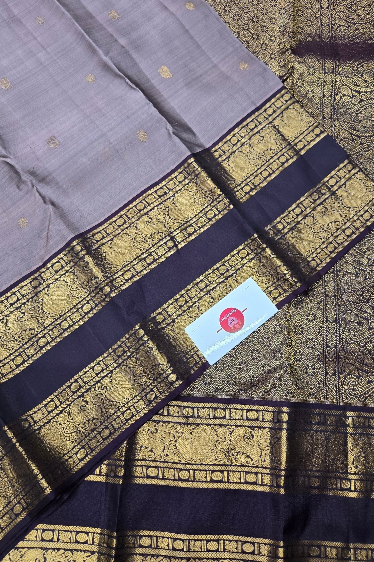 Gray saree with gold and black border and a visible brand label.