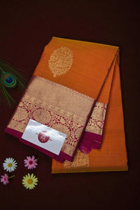 Orange saree with gold and maroon border on a dark brown background