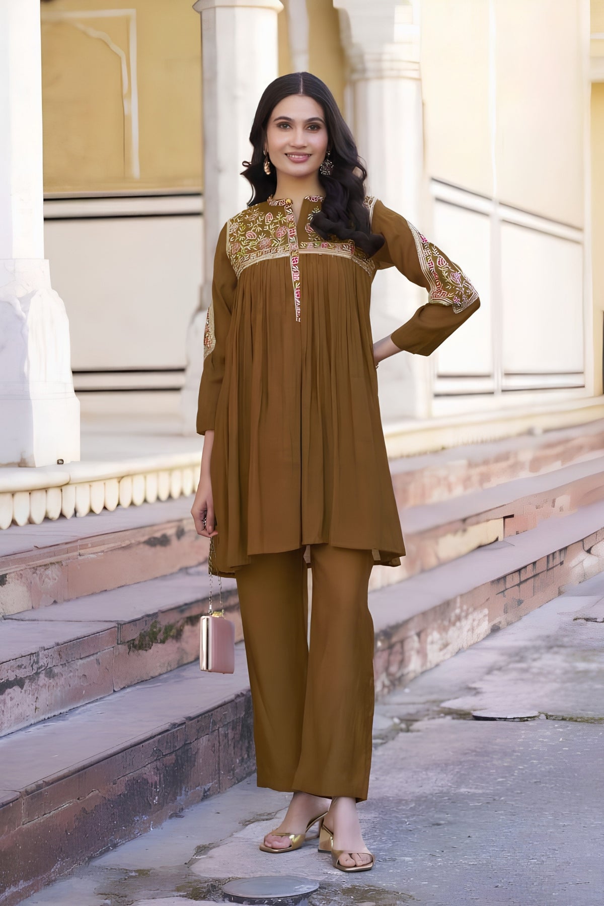 Woman in a brown traditional outfit standing in front of architectural steps.