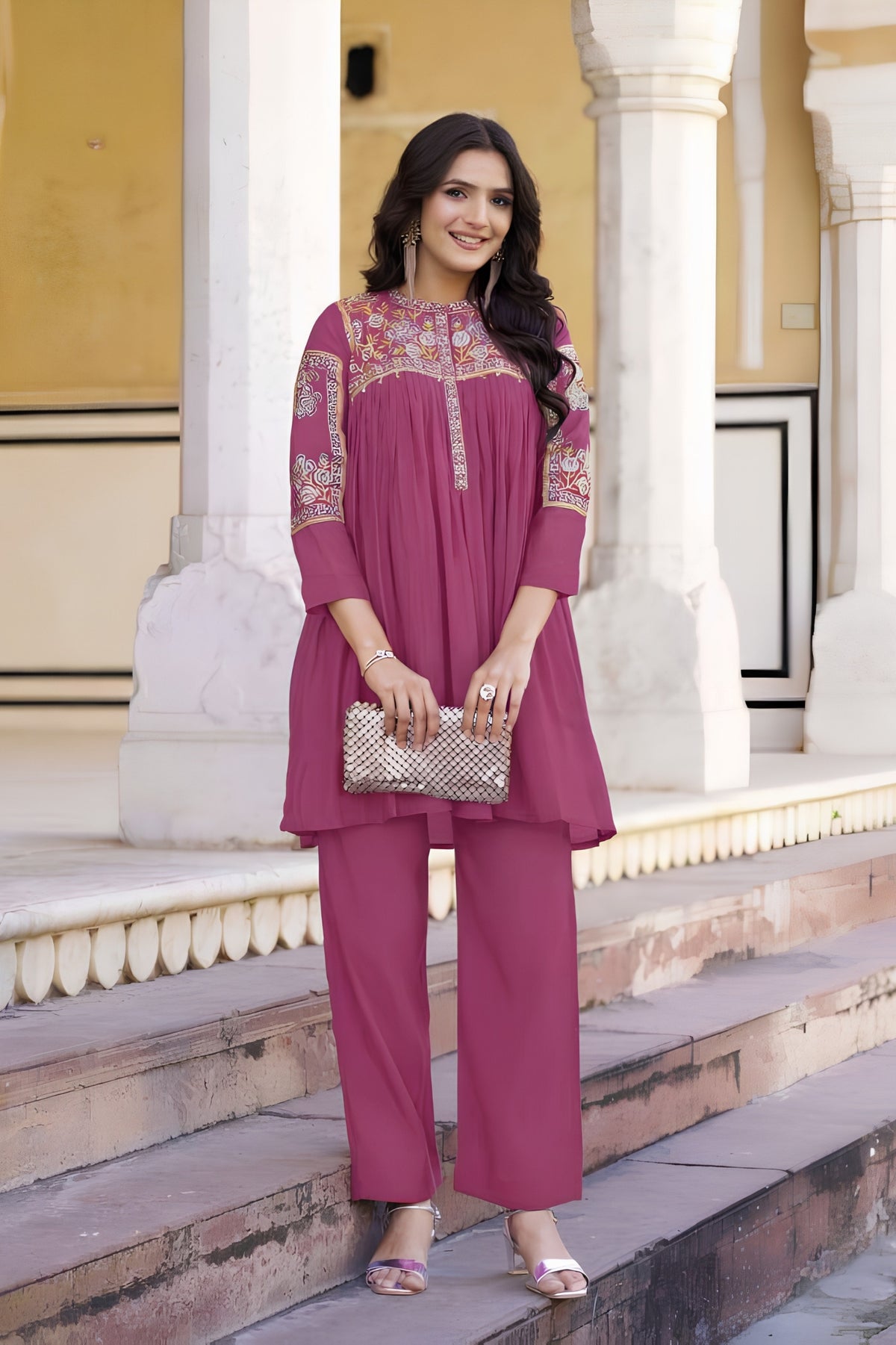 Woman in a pink traditional outfit standing on steps with classical architecture in the background