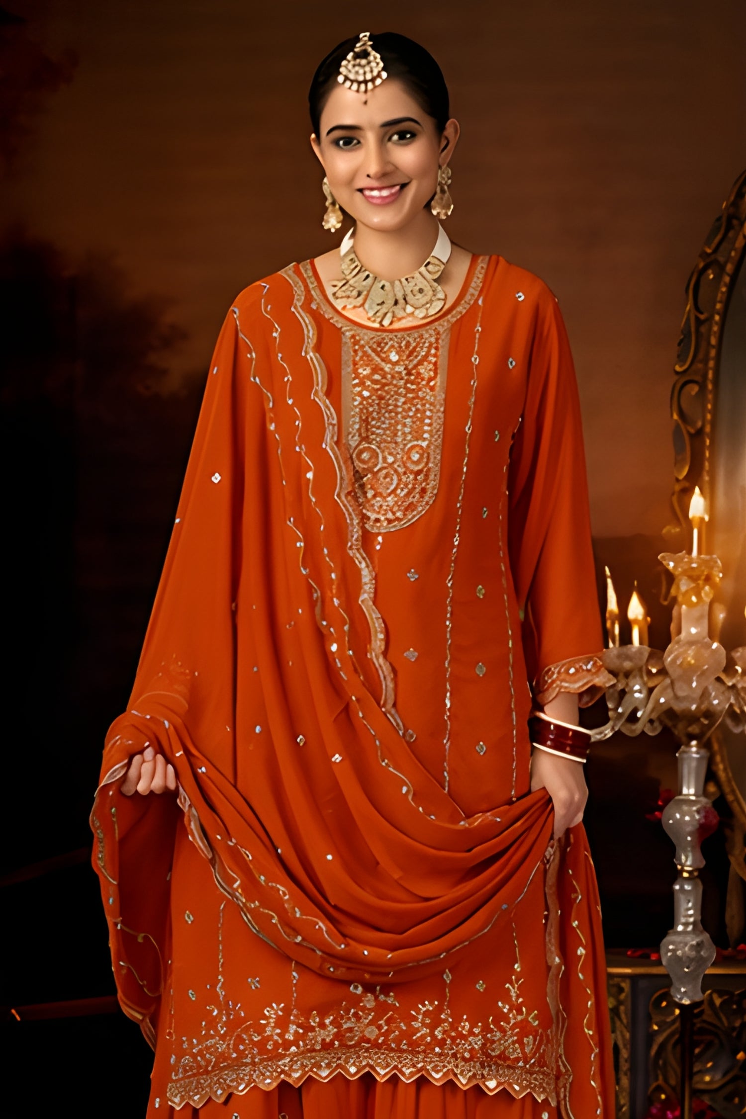 Woman in an orange embroidered traditional outfit with jewelry, standing against a dark background.