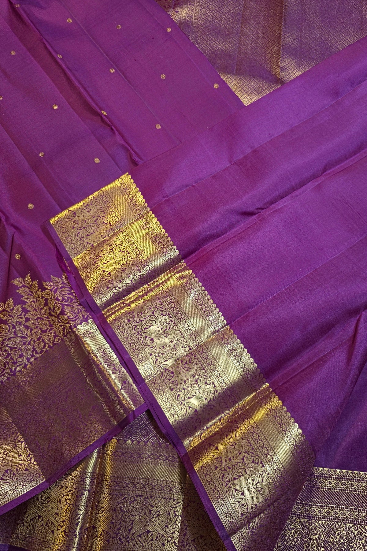 A close-up of a purple silk saree with a wide, ornate gold zari border and matching gold motifs.
