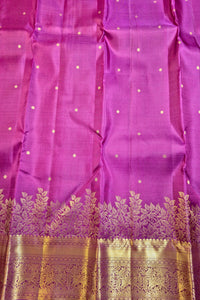 A close-up of a purple silk fabric, likely a sari, featuring small gold dot motifs and a wide ornate gold zari border at the bottom.