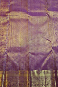 A close-up of a purple silk fabric with intricate gold zari woven patterns and a decorative border.