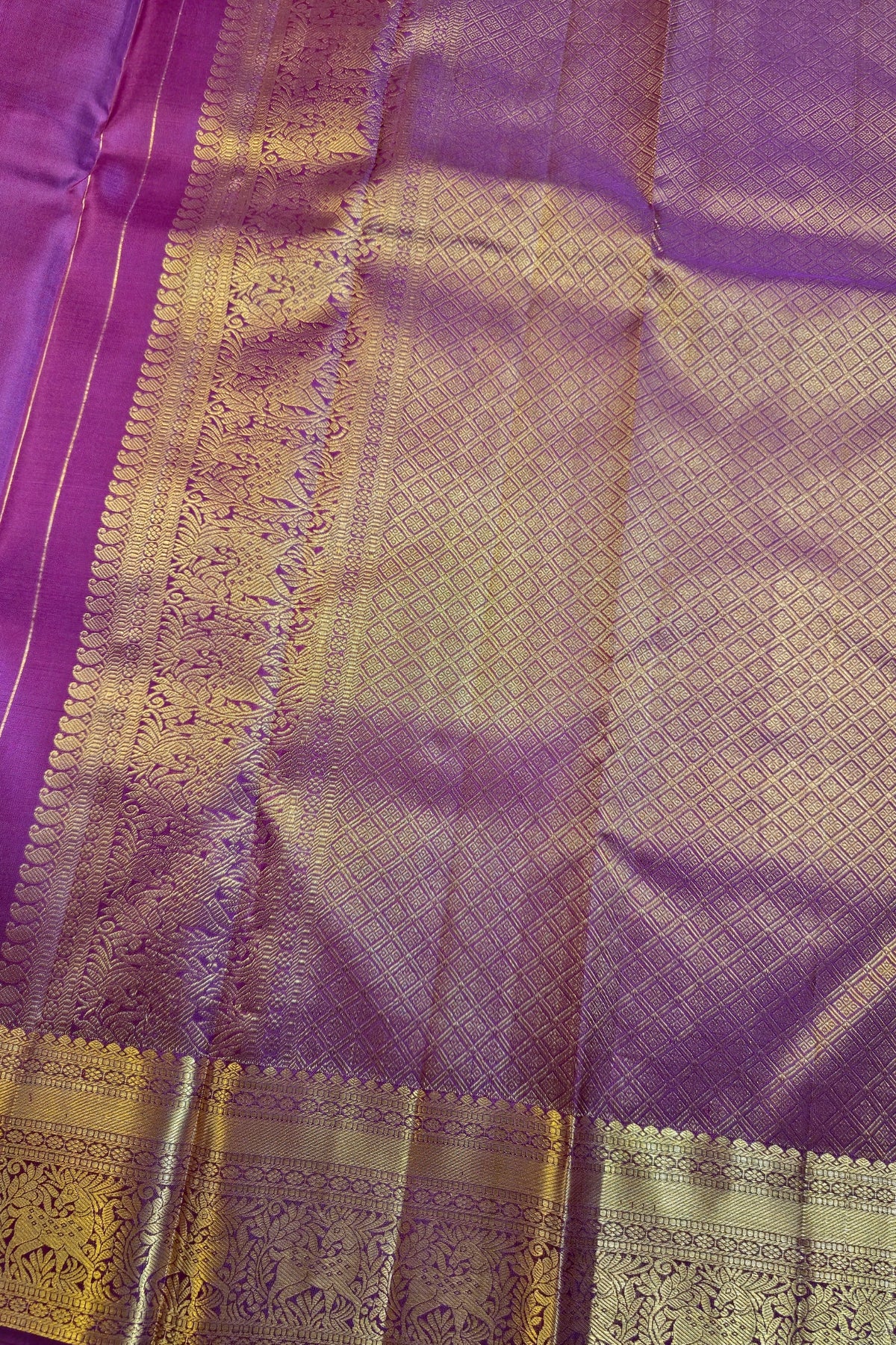 A close-up of a purple silk saree with intricate gold zari woven patterns and borders.