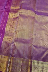 A close-up of a purple silk saree with intricate gold zari woven patterns and borders.
