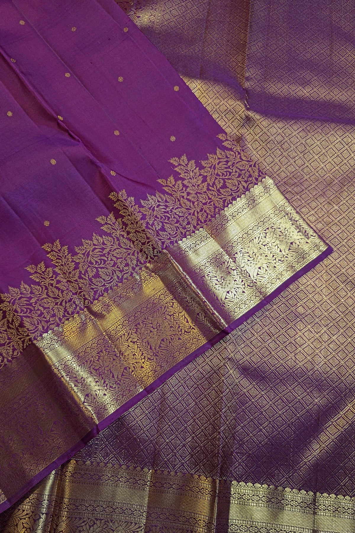 Purple silk saree with intricate gold zari brocade work and a wide decorative border, shown in a close-up diagonal layout.