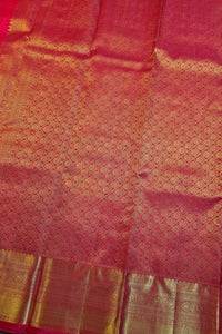 A close-up of a pink and gold woven fabric, likely a sari, featuring a repeating geometric pattern and a wide metallic gold border.