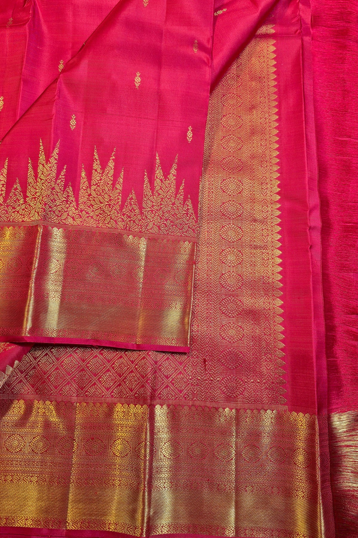 A close-up of a bright pink silk saree with intricate gold zari woven patterns and borders.