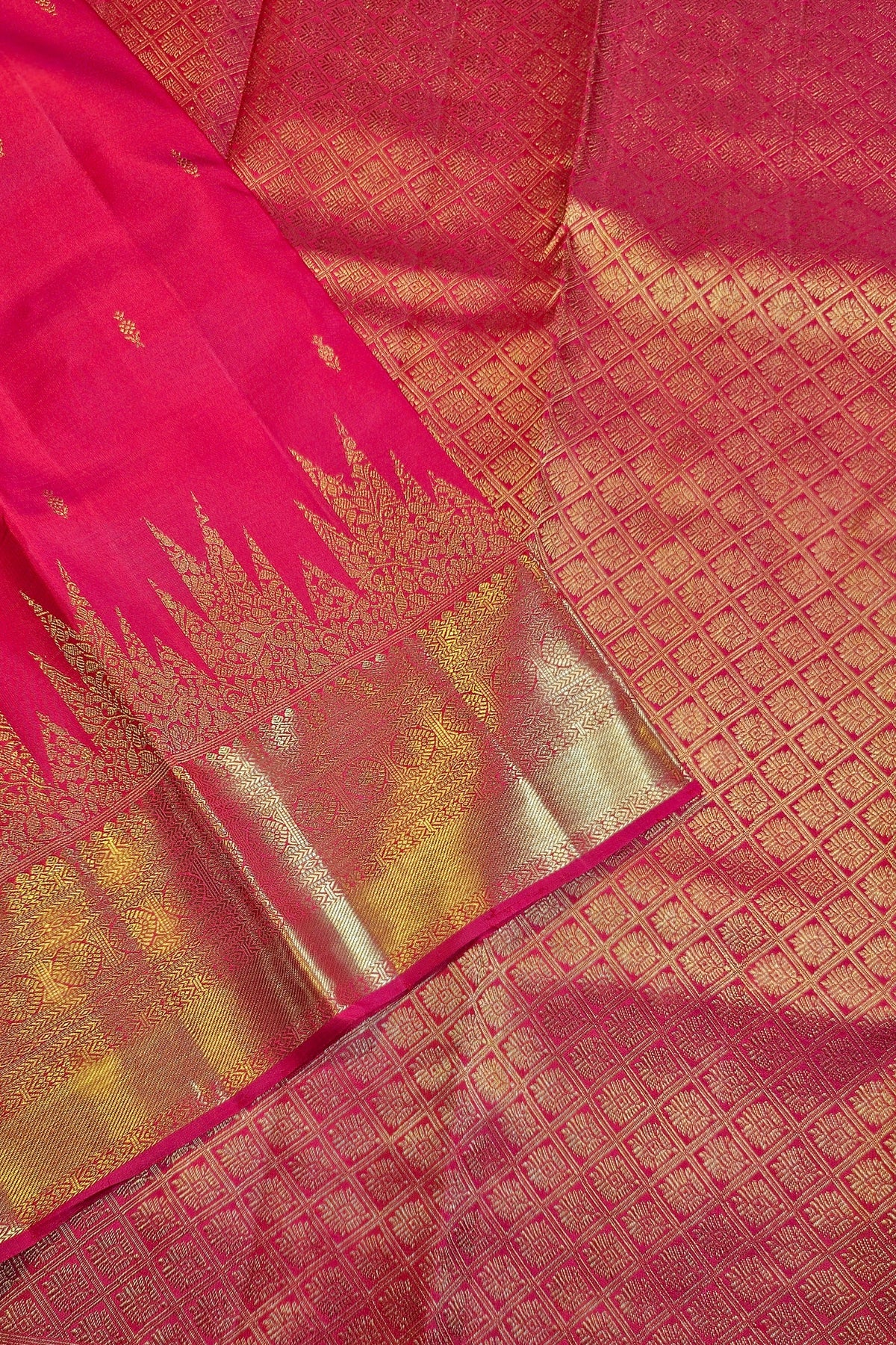 A close-up of a pink and gold zari woven fabric, likely a silk saree, showing the rich texture, geometric patterns, and a wide metallic gold border.