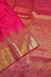 A close-up of a pink and gold zari woven fabric, likely a silk saree, showing the rich texture, geometric patterns, and a wide metallic gold border.