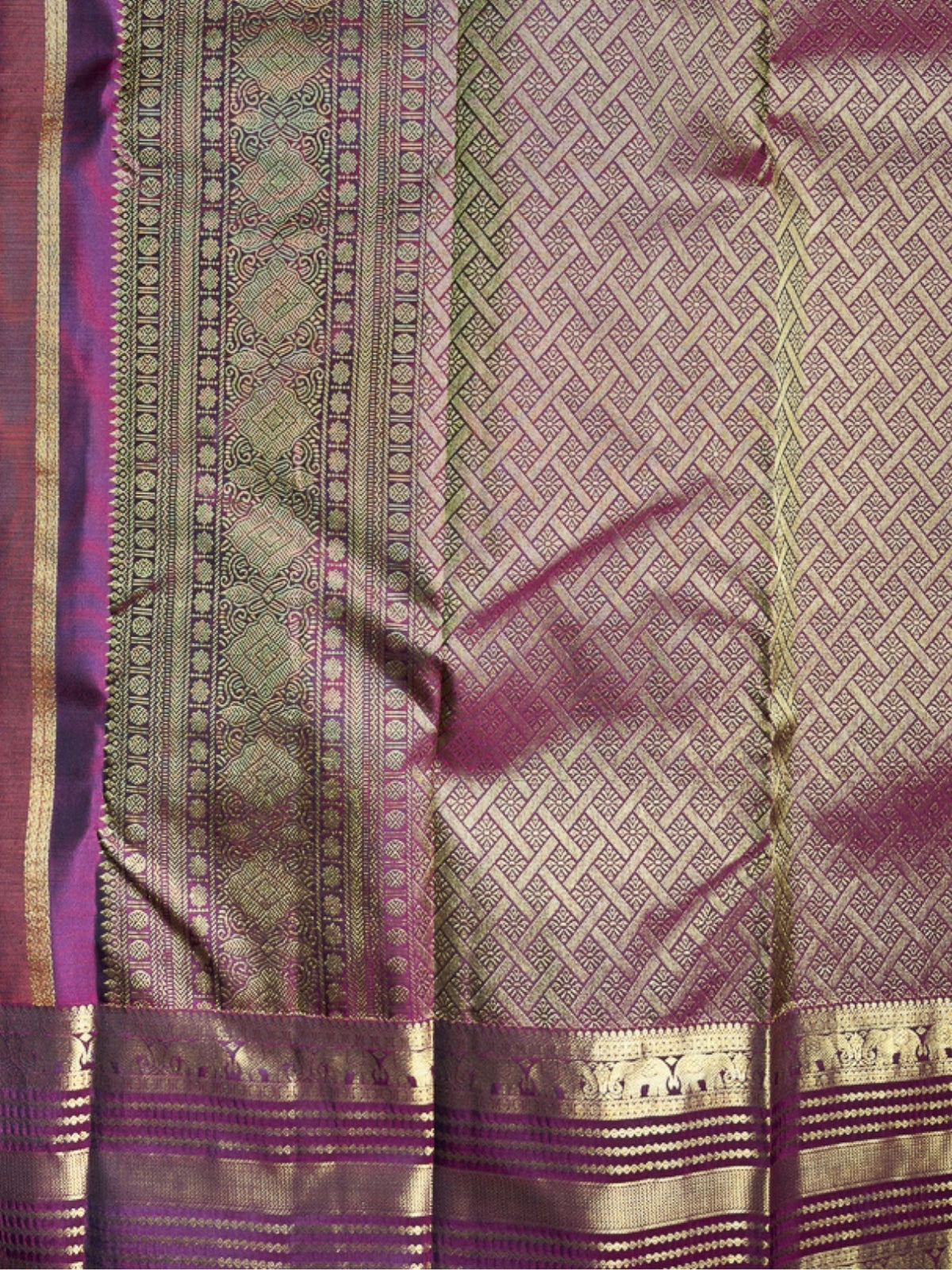 A close-up of a woven textile, likely a sari, featuring a metallic gold and purple geometric pattern with a wide purple border and ornate gold zari detailing.