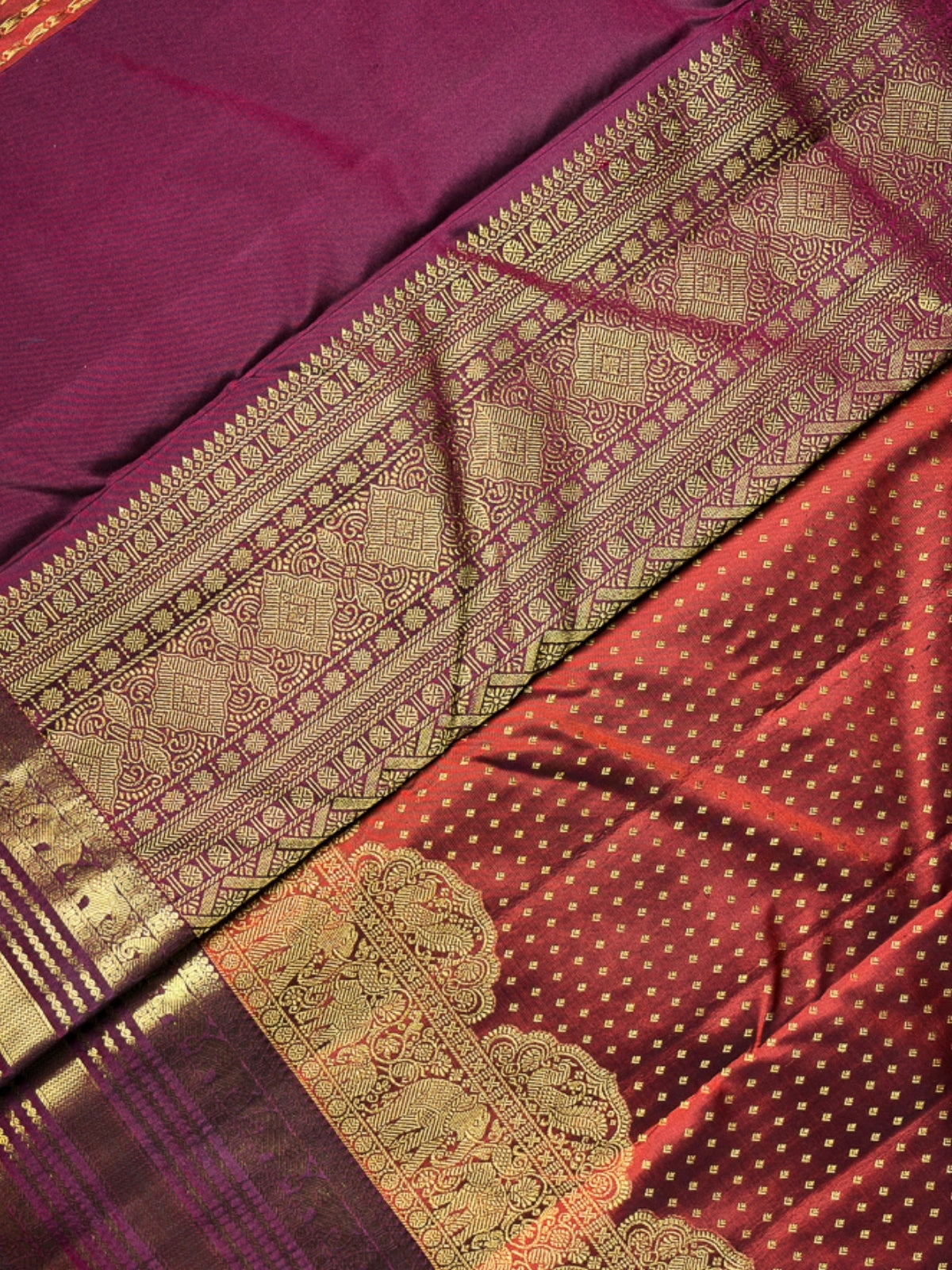 A close-up of a traditional Indian silk saree, showing the rich magenta-purple body, the detailed gold zari border, and the red-orange pallu with gold motifs.