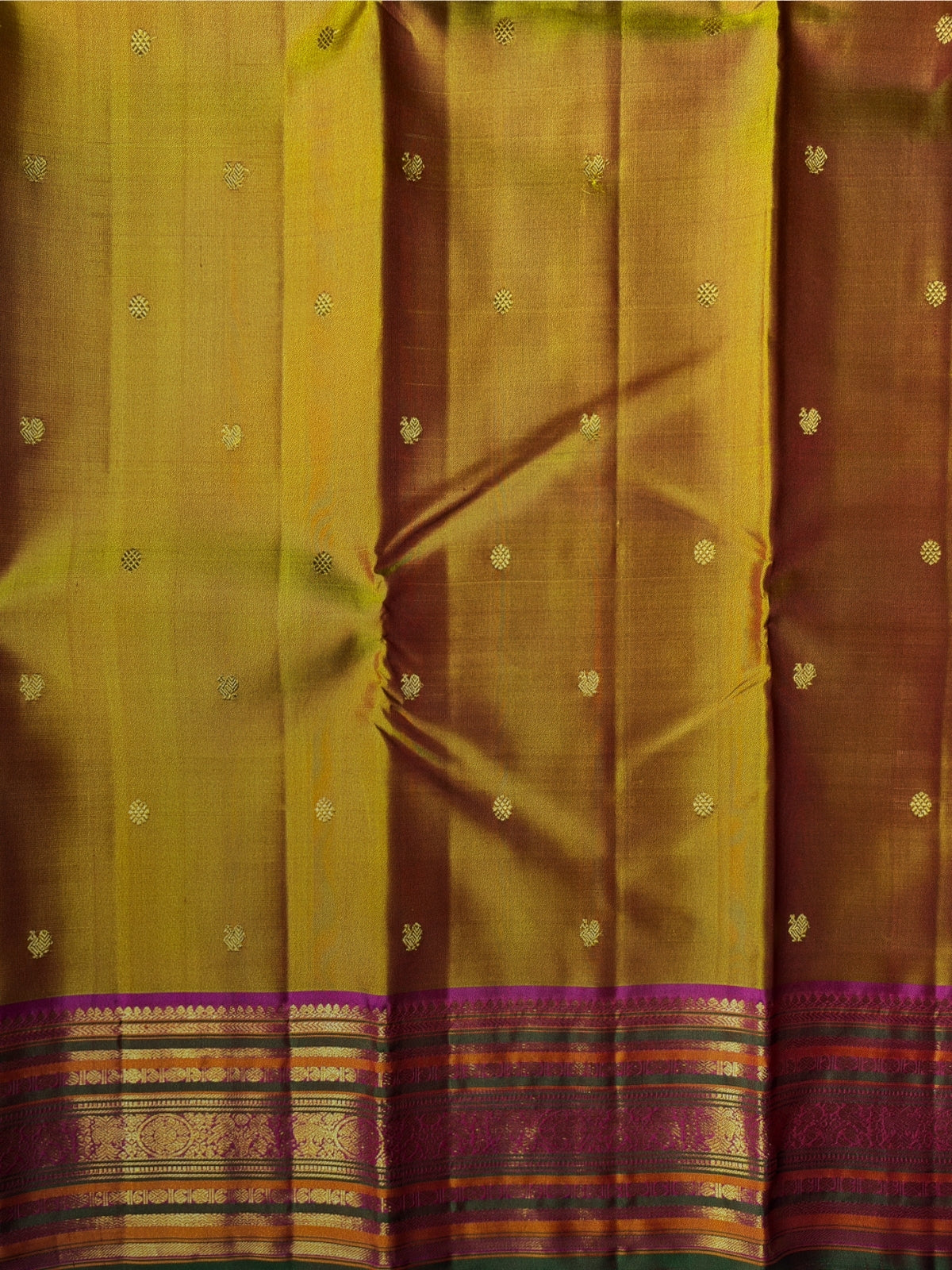 A close-up of a golden-yellow and brown silk saree body with small metallic zari motifs and a highly detailed, multicolored zari border at the bottom.