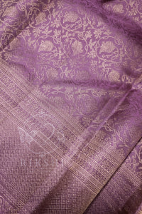 A close-up of a purple silk fabric with intricate gold zari brocade patterns and a detailed border.