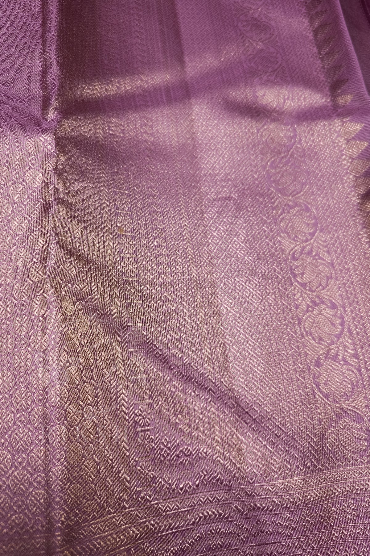 A close-up of a lavender purple woven fabric with metallic gold zari patterns and borders.