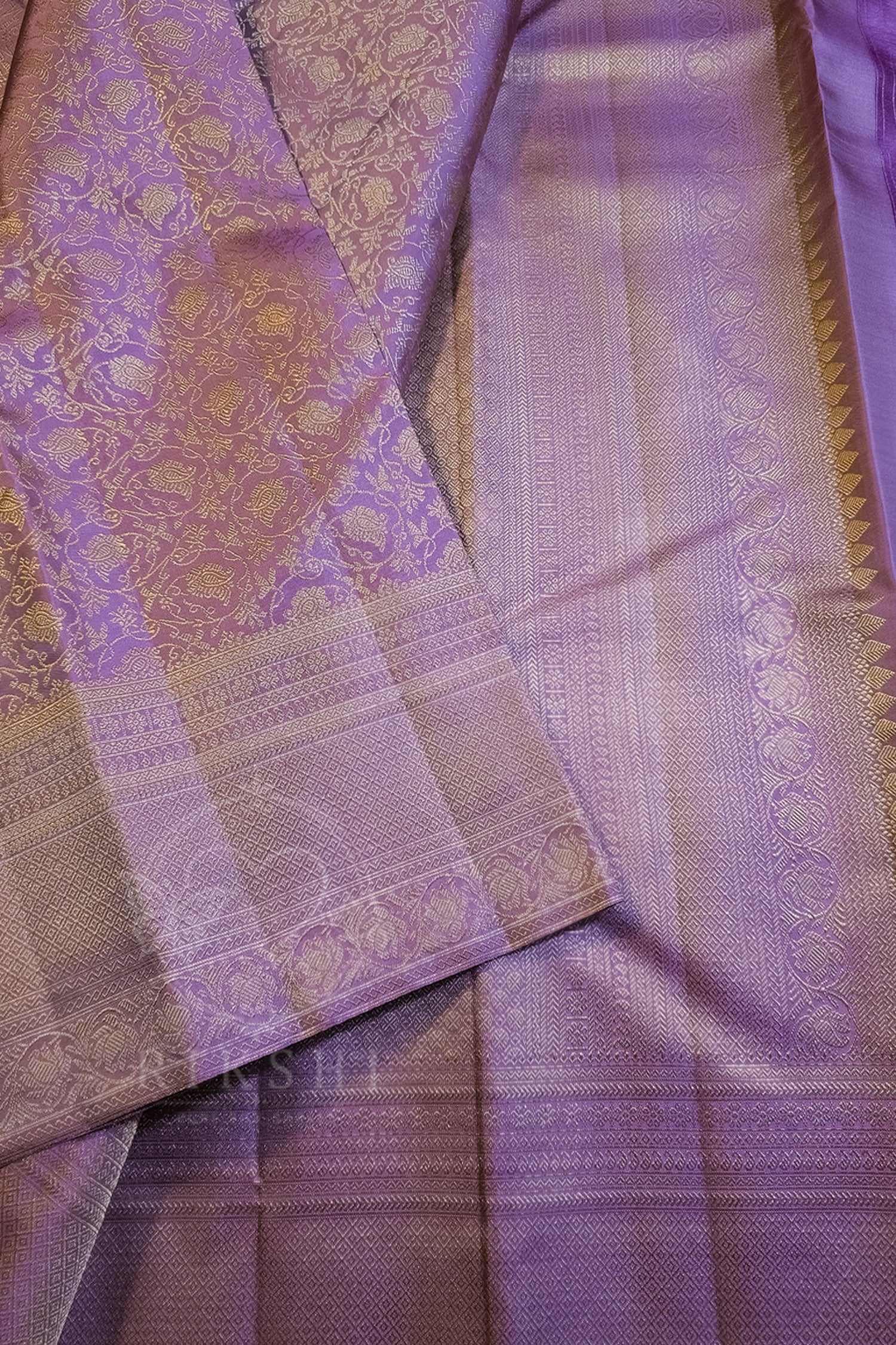 A close-up of a lavender purple silk saree with intricate gold zari brocade patterns and borders.