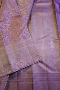 A close-up of a lavender purple silk saree with intricate gold zari brocade patterns and borders.
