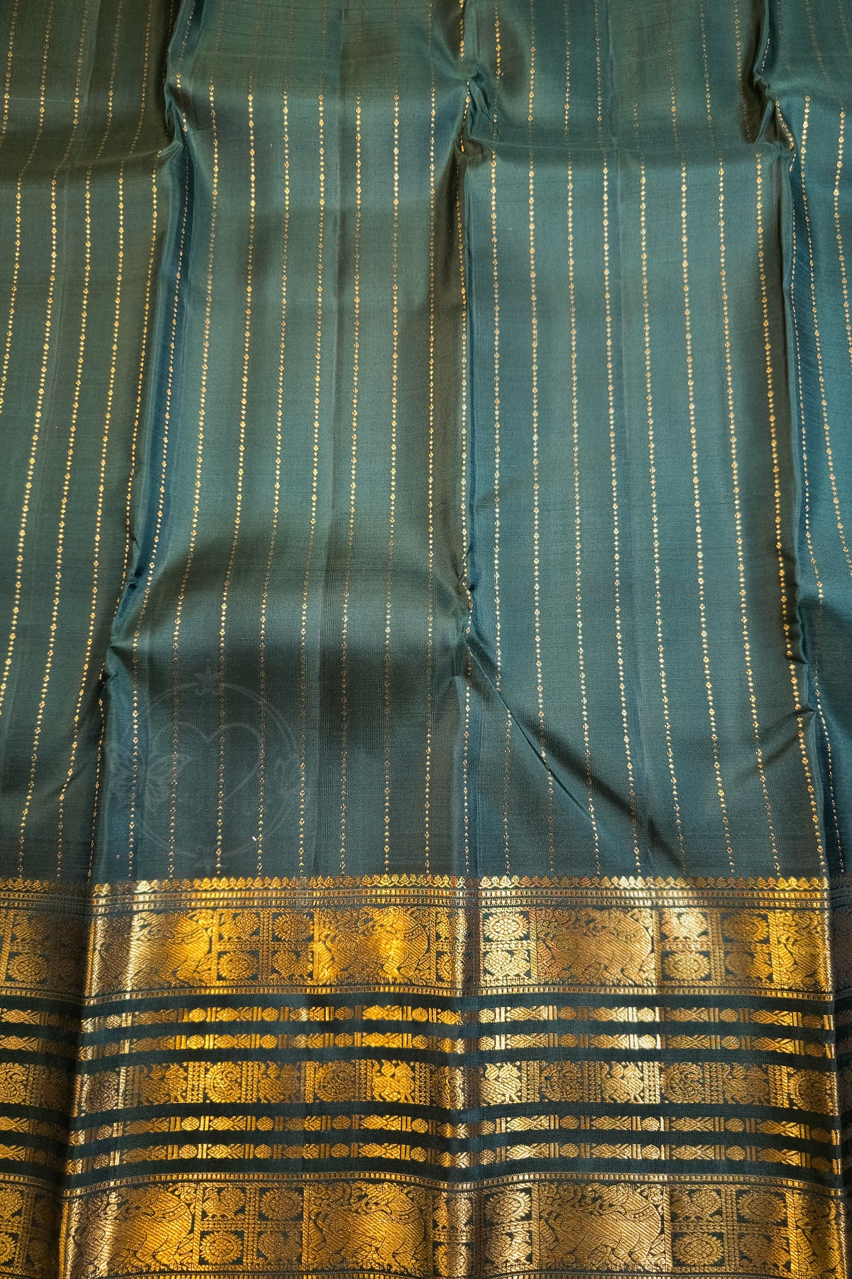 A close-up of a teal blue-green fabric with fine vertical gold stripes and a wide ornate gold zari border at the bottom.