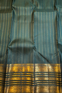A close-up of a teal blue-green fabric with fine vertical gold stripes and a wide ornate gold zari border at the bottom.