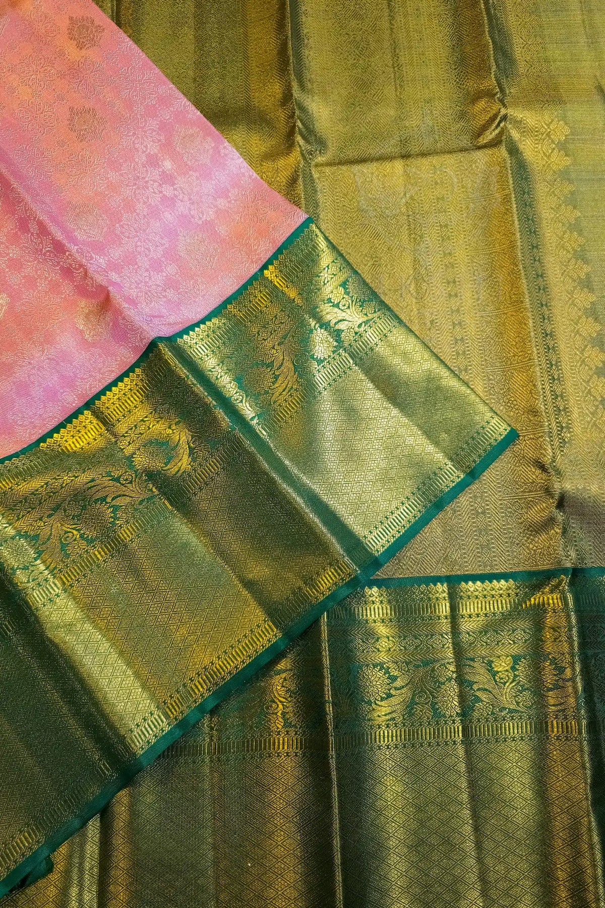 A close-up of a traditional Indian silk saree, showing a pink floral-detailed pallu and a metallic gold body with a wide green and gold zari border.