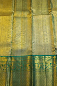 A close-up of a woven fabric, likely a silk saree or scarf, featuring a metallic gold body with a teal green border and intricate floral patterns.