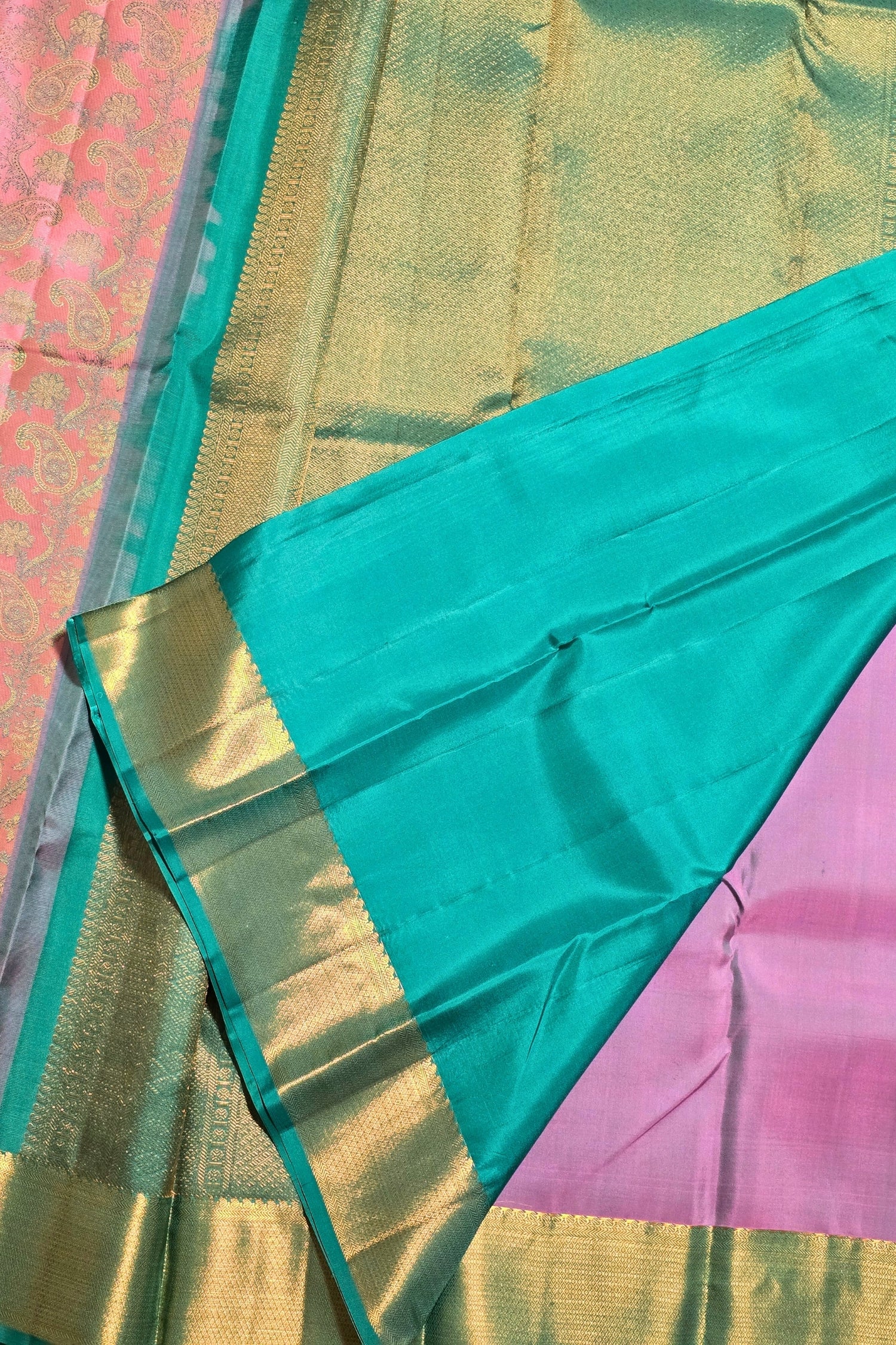 Teal saree with gold border on a pink fabric background