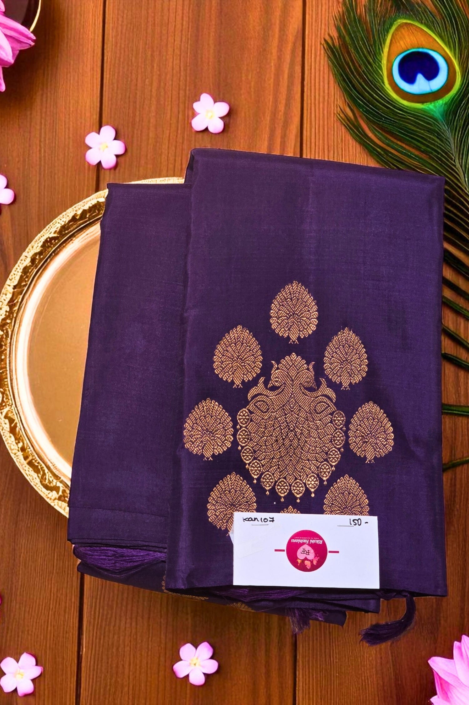 Purple fabric with gold embroidery on a wooden surface with peacock feather and flowers.