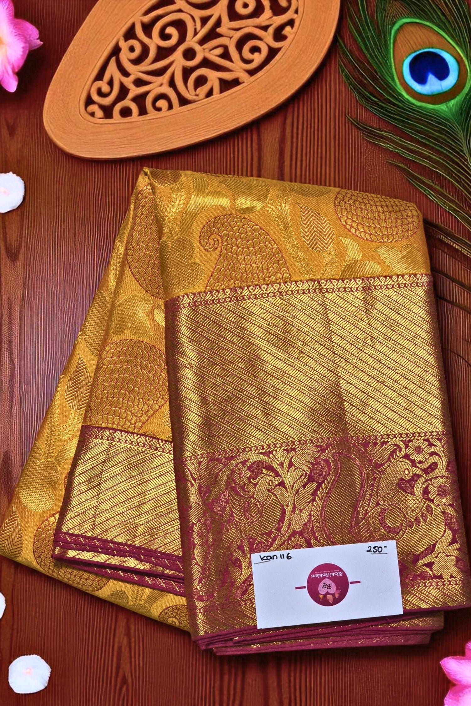 Gold saree with intricate patterns on a wooden surface with peacock feather and decorative item.
