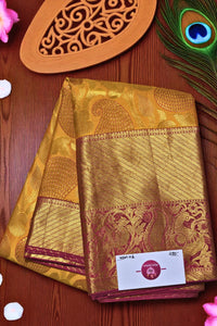 Gold saree with intricate patterns on a wooden surface with peacock feather and decorative item.