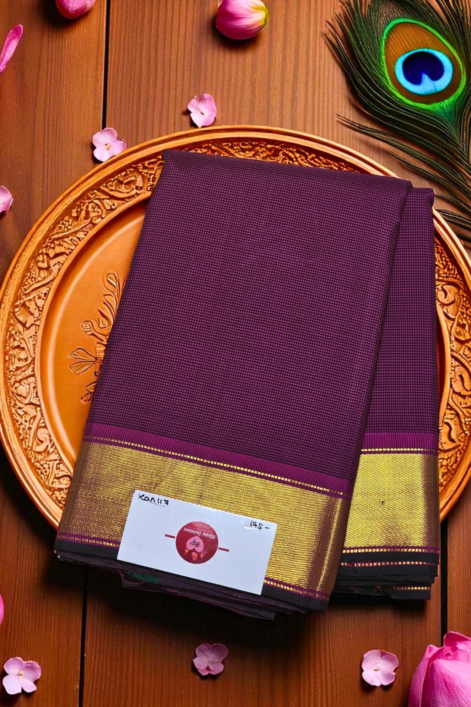 Purple saree with gold border on a decorative plate, surrounded by pink petals and a peacock feather.