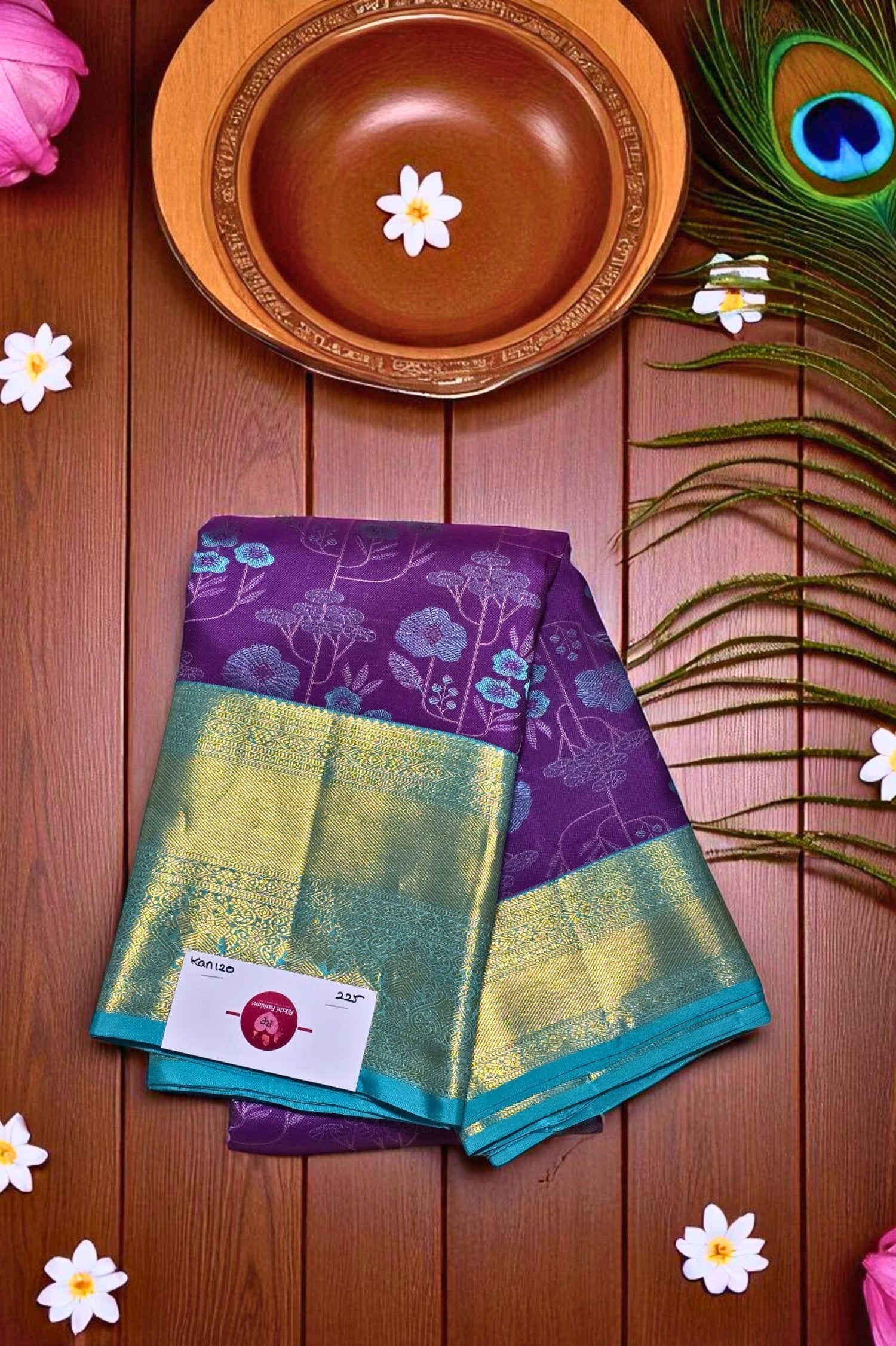 Purple and green fabric with a floral pattern on a wooden surface with flowers and a peacock feather.