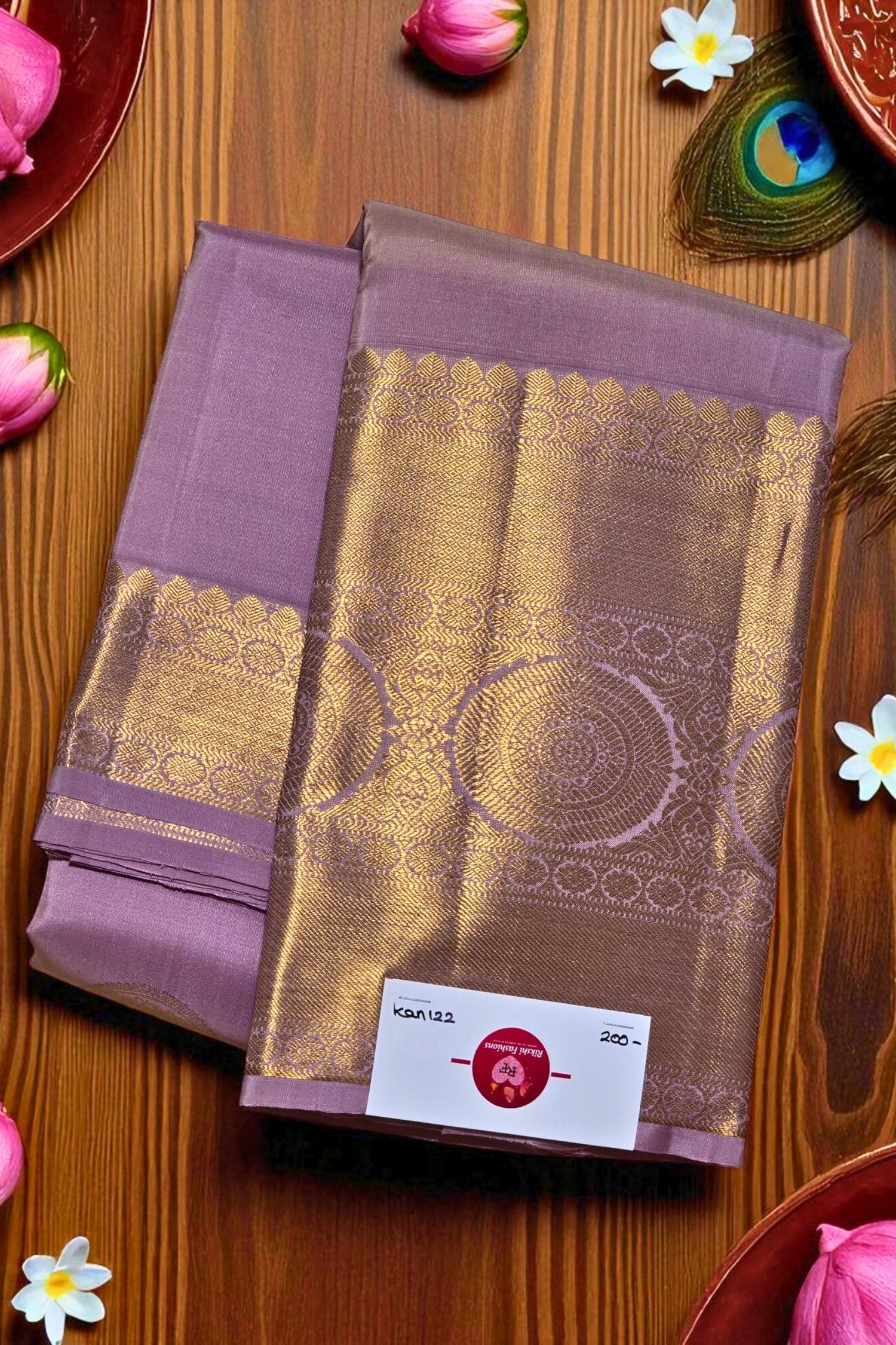 Purple and gold saree with a brand label on a wooden surface with decorative elements.