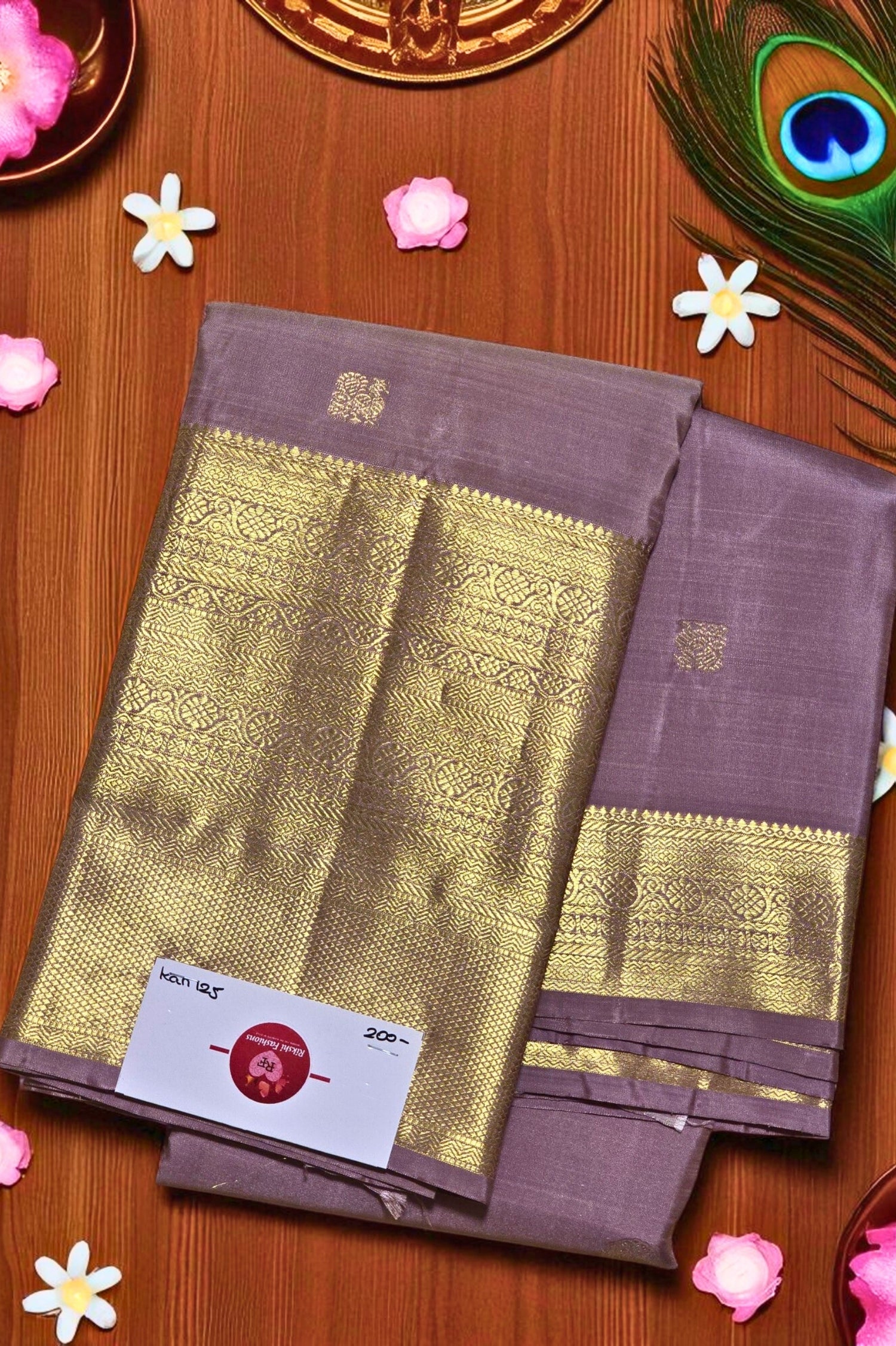 Brown saree with gold border on a wooden surface with flowers and a peacock feather.
