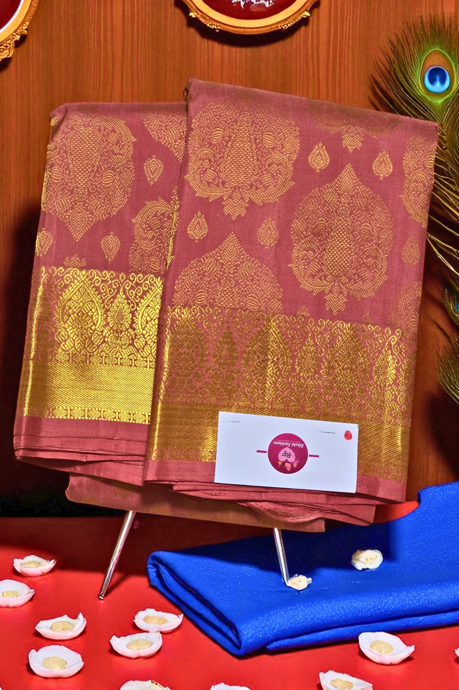 Two pink sarees with gold patterns on a stand against a wooden background.