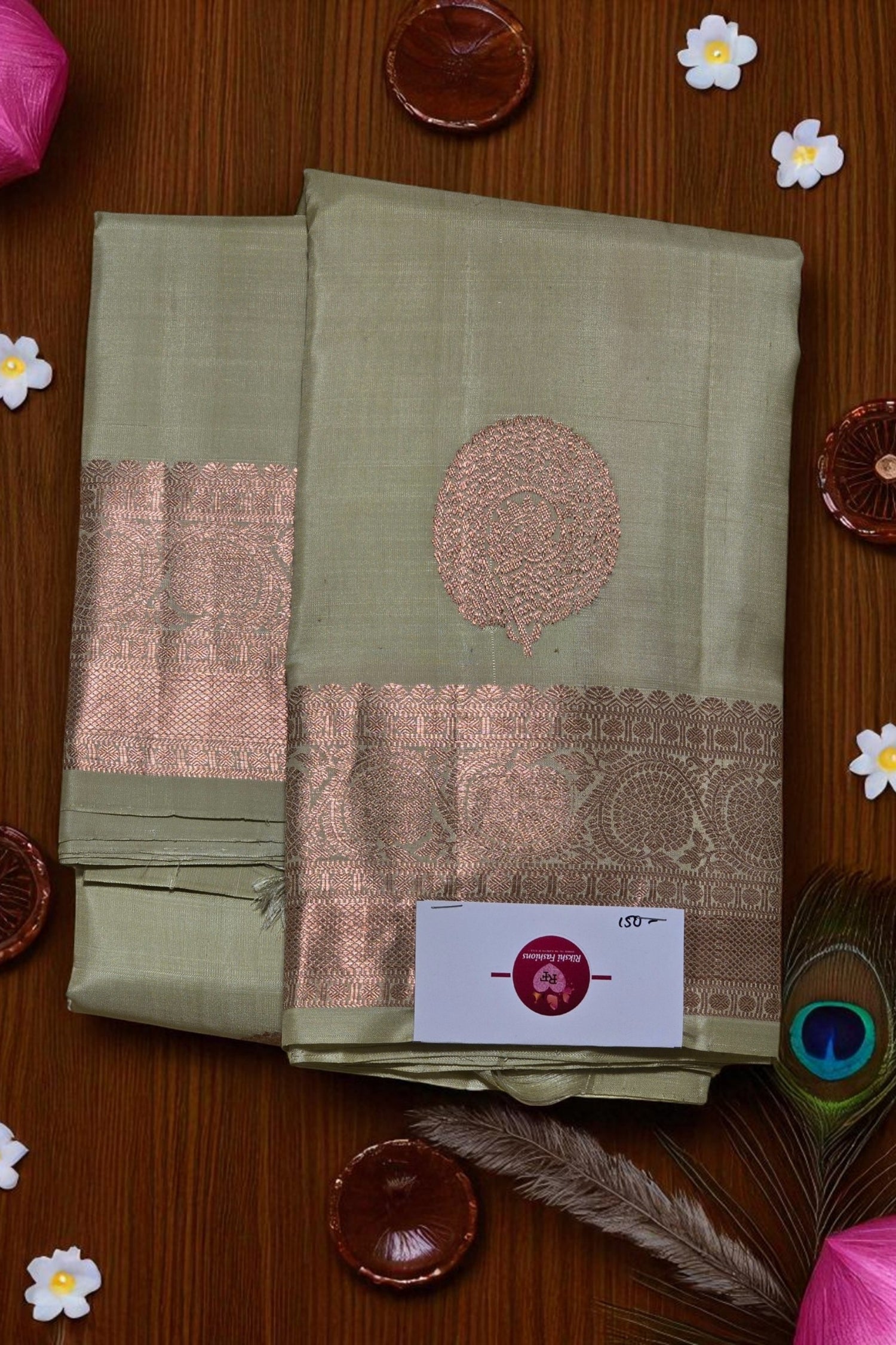 Green saree with pink border on a wooden surface with decorative items
