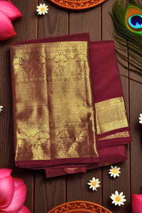Maroon saree with gold border on a wooden surface with decorative elements