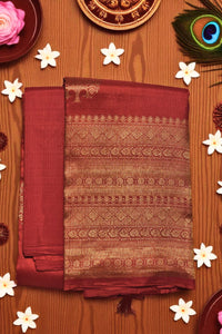 Maroon saree with gold patterns on a wooden background with flowers and a peacock feather.