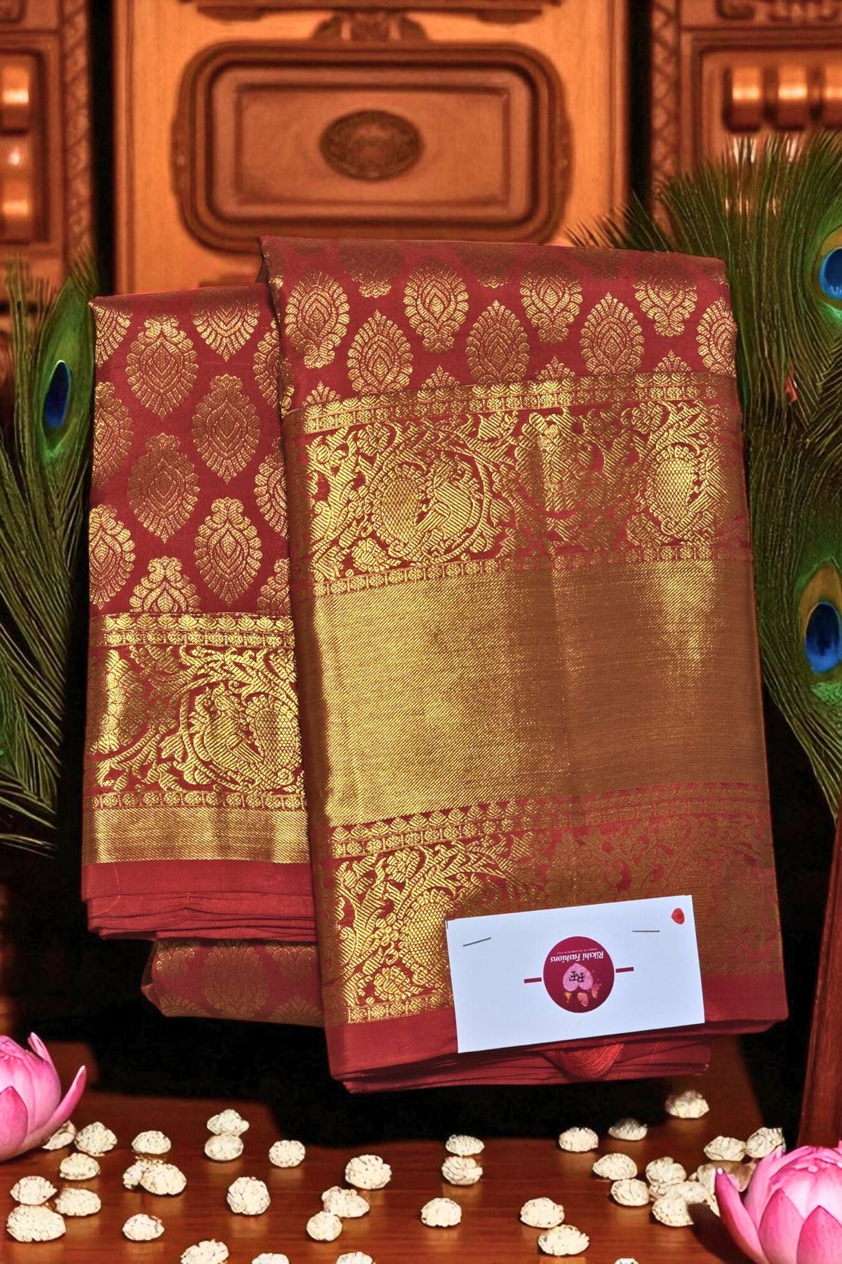 Red and gold saree with intricate patterns on a wooden background with peacock feathers and lotus flowers.