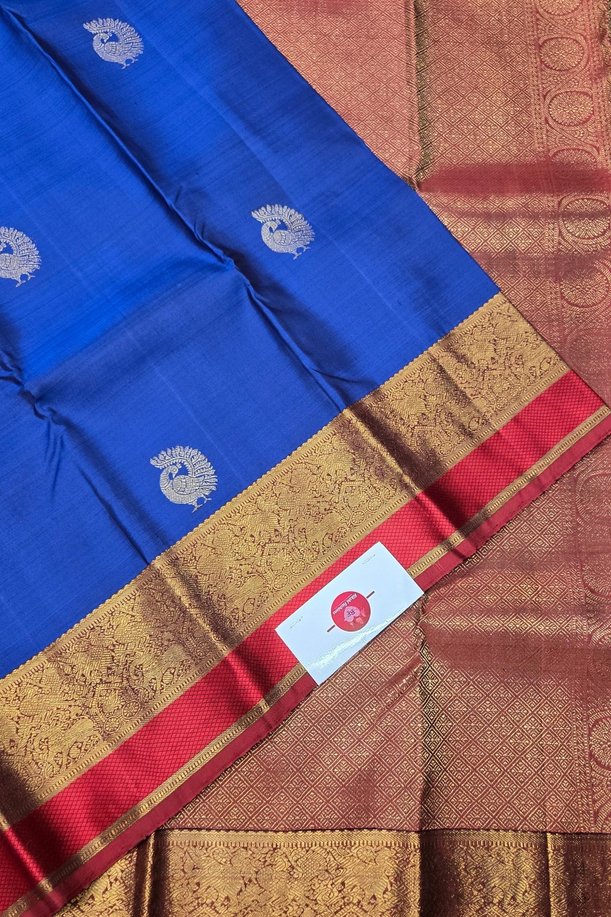 Blue saree with gold and red border featuring a brand label.
