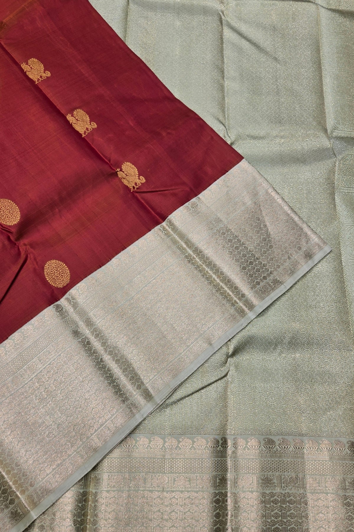 Saree with maroon border and gold embroidery on a light gray background