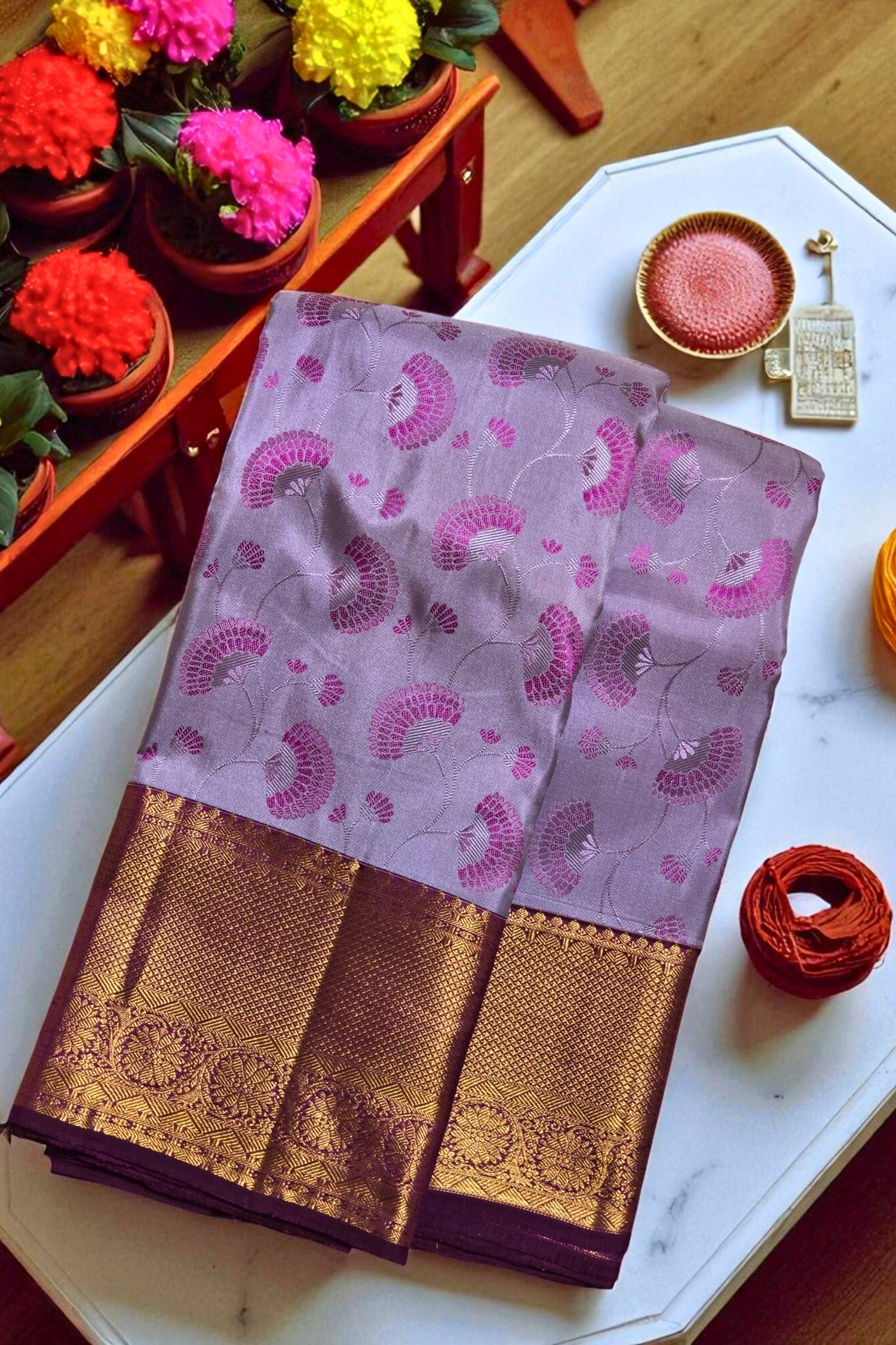 Purple saree with gold border on a white surface, surrounded by decorative items.