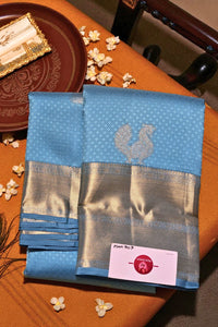 Blue saree with silver zari border on a wooden table with decorative elements.