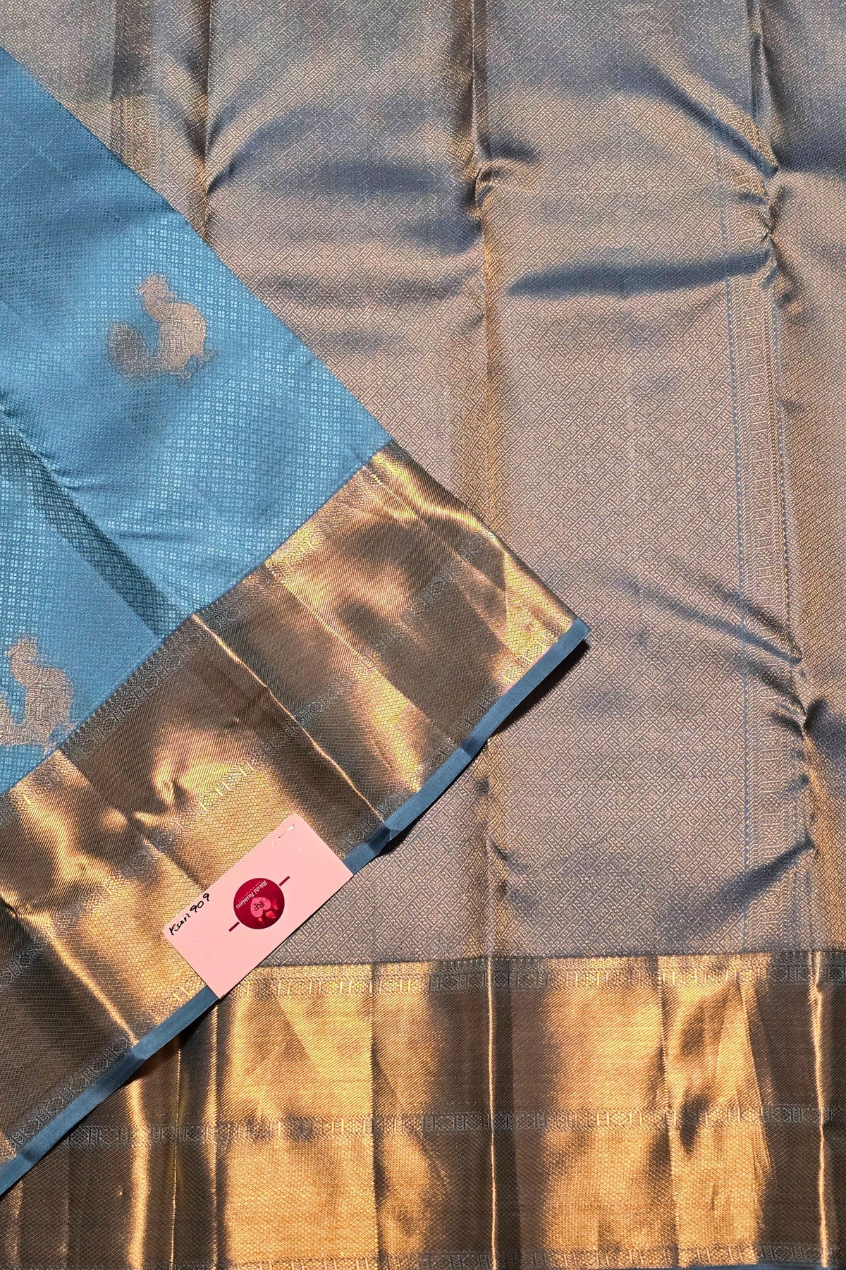 Close-up of a fabric with a gold and blue pattern, featuring a pink tag.