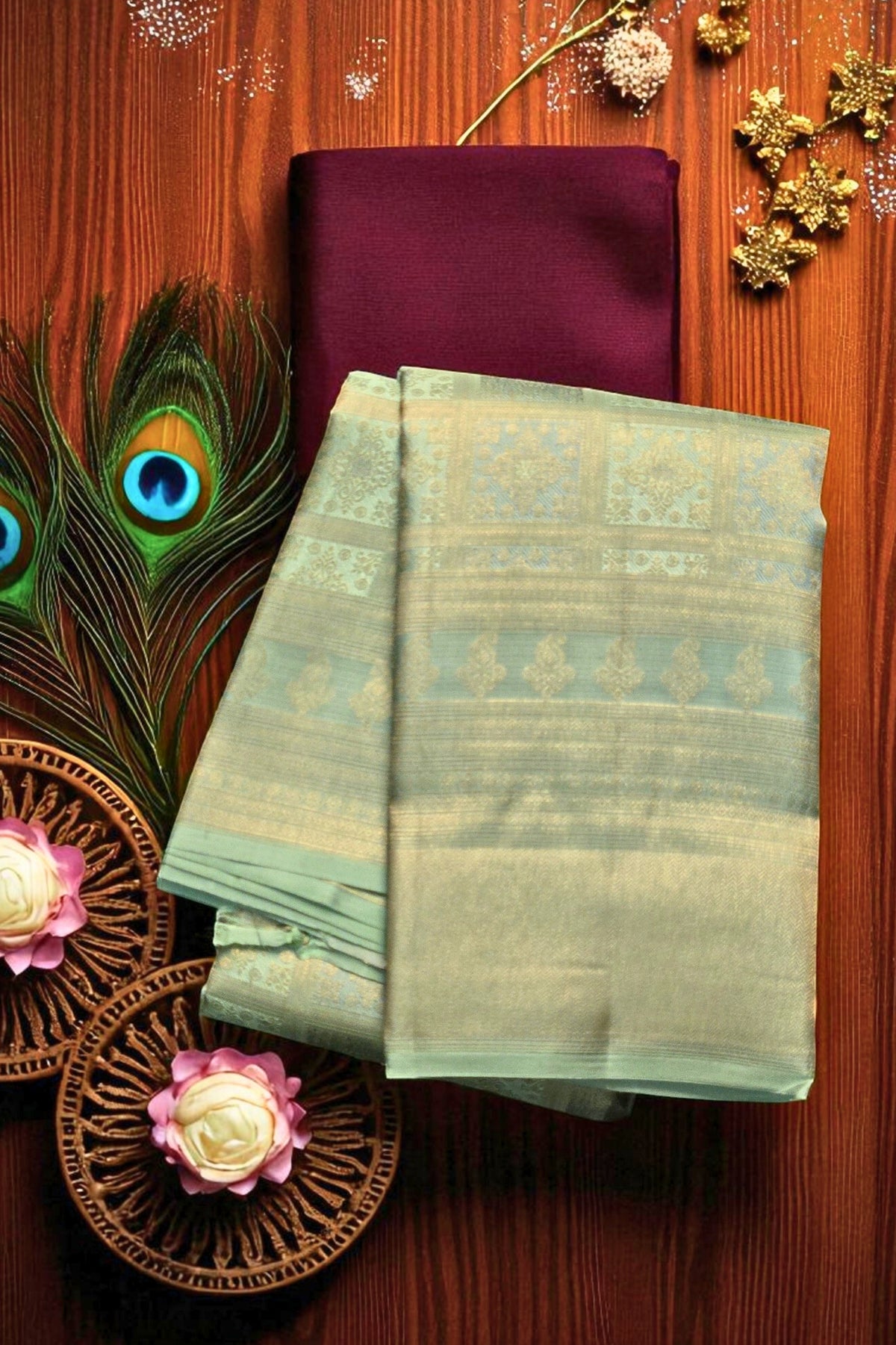 Two green sarees on a wooden surface with decorative elements including a peacock feather and flowers.