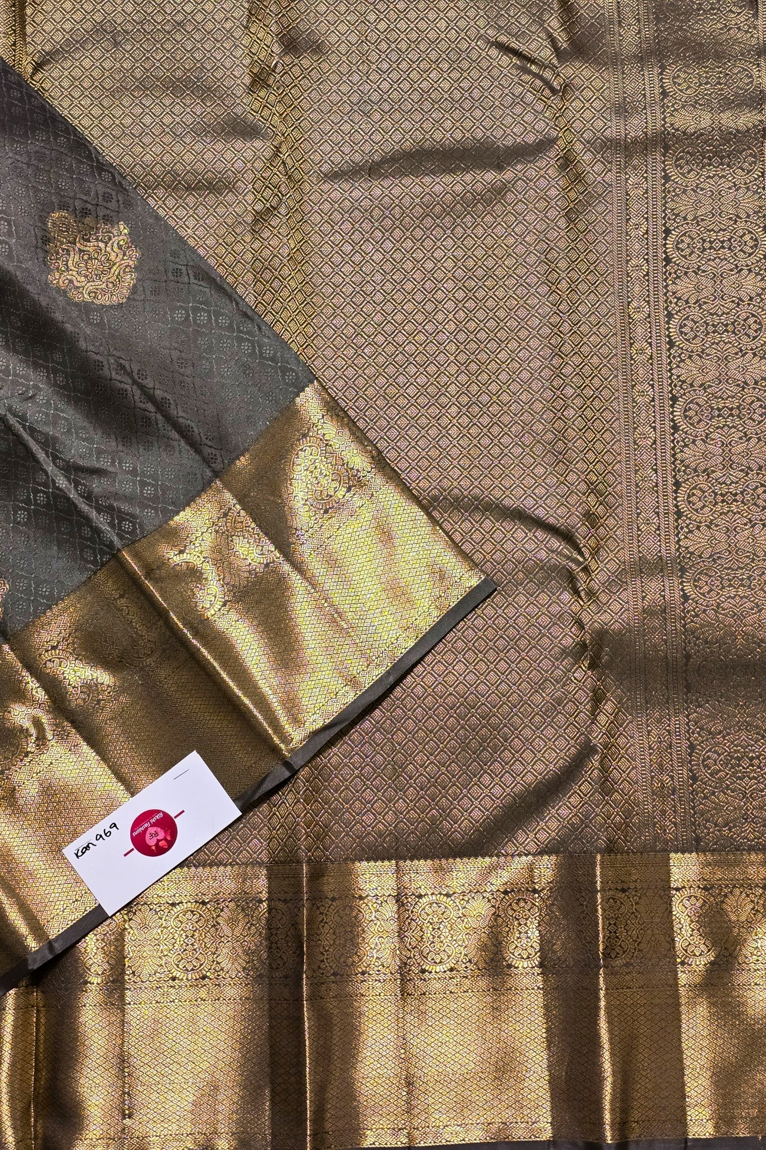 Close-up of a traditional fabric with gold and black patterns, featuring a brand label.