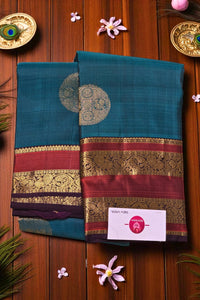Two teal sarees with decorative borders on a wooden background with flowers and decorative items.
