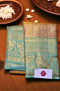 Teal and gold saree with a brand label on a wooden surface
