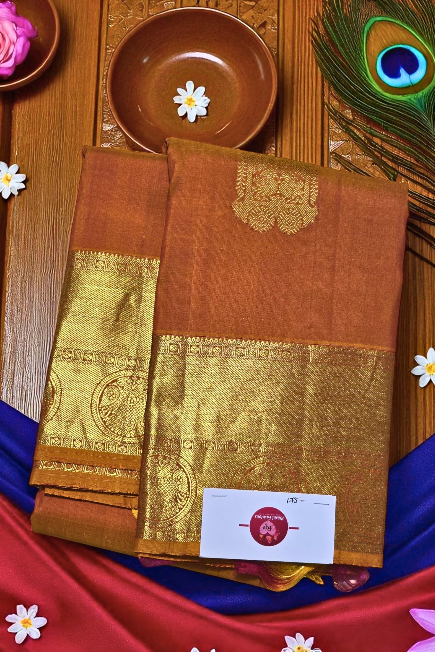 Brown and gold saree with a brand label on a wooden surface with decorative elements.