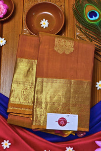 Brown and gold saree with a brand label on a wooden surface with decorative elements.